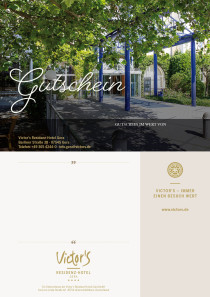 Der Hoteleingang ist in der Bildmitte. Das Sonnenlicht scheint durch den großen Baum vor der Einfahrt.