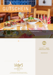 Die Victor's Stube mit hölzernen Tischen und Stühlen sowie rot-weiß-karierten Kissen laden zum Essen ein. Im Hintergrund steht ein Kamin.