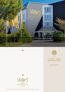 Die Hotelfassade ist zu sehen. Der Himmel leuchtet blau. Vor dem Hotel stehen Bäume und goldene Victor's-Fahnen wehen im Wind.