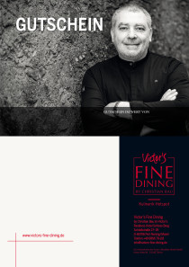 Lächend lehnt Christian Bau, gekleidet in eine schwarze Kochjacke, an einer Steinwand.