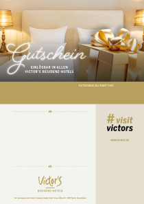 Ein beiges Geschenk mit goldener Schleife vor einem beigen Bett mit weißen Kissen. Die Nachtschränke mit Lampen sind auch in beige gold gehalten.