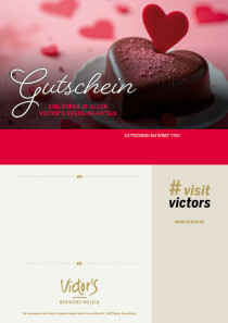 Ein Schokoladenkuchen in Herzform ist mit einem kleinen roten Steckherz dekoriert. Im Hintergrund liegen auf einer zart roten Tischdecke weitere rote Herzen als Deko.